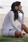 Jeune femme assise sur la plage, écouter de la musique, la main sur le menton