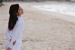Jeune femme debout sur la plage, les mains derrière le dos, à la recherche de suite