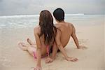 Couple assis sur la plage, face à la mer