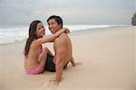 Couple sitting on beach, embracing, looking at camera