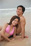 Couple sitting on beach, looking at camera, portrait