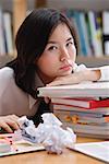Young woman in library, leaning on books, sad expression