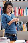 Young woman in library, using mobile phone, looking at camera