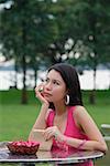 Young woman sitting at outdoor table, hand on chin, looking away