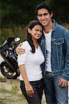 Young couple with motorbike smiling at camera