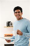 Young man with coffee and paper smiling at camera