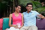 Couple sitting on sofa outdoors, smiling at camera