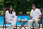 Couple sitting by the pool, looking at camera