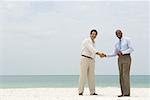 Two businessmen shaking hands on the beach, both smiling at camera