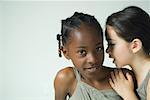 Girl looking at camera as friend whispers in her ear