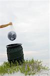 Person holding globe in plastic bag over garbage can, cropped view