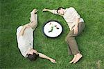 Two men lying on grass around bowl with flower, eyes closed