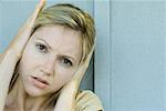 Woman covering ears with hands, frowning at camera