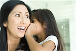 Girl whispering in mother's ear, close-up