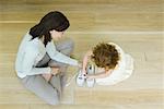 Mother and little girl sitting on floor, girl learning to tie shoe laces, view from directly above
