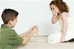 Boy stacking blocks while little sister watches, hand over mouth