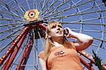 Female teenager on cell phone at Ferris wheel in amusement park