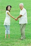 Grandfather and teenage granddaughter holding hands, both smiling over shoulders at camera