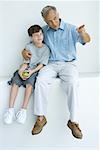 Man sitting with arm around grandson's shoulders, pointing, both looking away