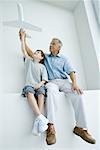 Grandfather and grandson sitting side by side, holding up toy airplane together