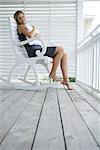 Femme assise dans le fauteuil à bascule sur le porche, étreindre oreiller, souriant à la caméra