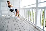 Femme assise dans le fauteuil à bascule sur le porche, étreindre oreiller, loin à la recherche