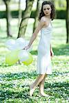 Jeune femme qui marche dans le champ de fleurs, tenant des ballons derrière le dos, regarder par-dessus l'épaule