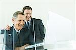 Businessman looking over colleague's shoulder at laZSop computer, both smiling, low angle view