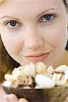 Woman holding up bowl of flowers, smiling at camera, close-up