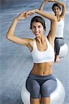 Teenage twin sisters sitting on fitness balls, arms raised, both smiling