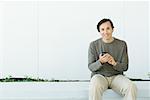 Man sitting, holding cell phone, smiling at camera