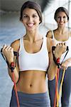 Teenage twin sisters exercising with resistance bands, both smiling at camera