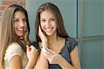 Teenage twin sisters listening to mp3 player together, both smiling, one looking at camera