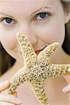 Young woman holding up starfish, smiling at camera, focus on foreground