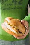 Hand holding sausage and mustard in a bread roll