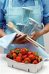 Woman with preserving jars, kitchen spoons & strawberries