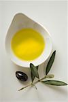 Olive oil in bowl, olive and olive branch beside it