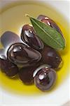 Olive oil, black olives and olive leaf in bowl