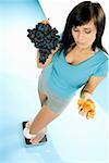 Young woman standing on scales with crisps and grapes