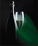 Bottle and glass of sparkling wine in green light