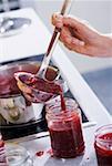 Raspberry jam being ladled into a screw-top jar