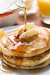 Pouring maple syrup over pancakes with dab of butter