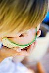 Small child biting into a slice of melon