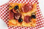 A slice of salami pizza with peppers and olives