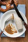 Cooked Weisswurst with mustard on plate, pretzel behind