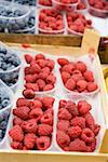 Raspberries and blueberries in plastic punnets at a market