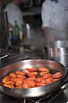 Tomatoes in frying pan on stove, chefs in background