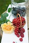 Fresh berries in basket and jar and yellow rose on table