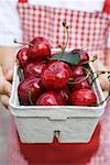 Hands holding cardboard punnet of fresh red cherries