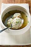 Clear broth with bacon dumplings in soup bowl with spoon